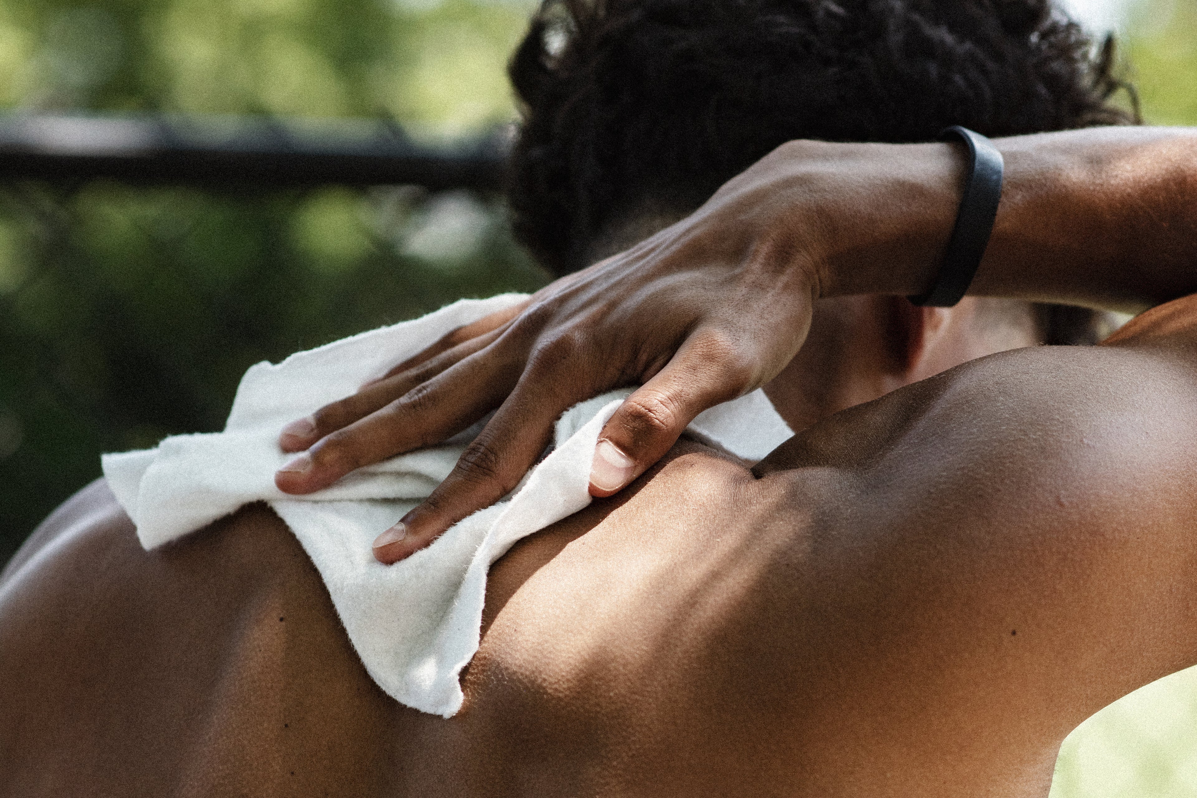 Close-up of a person using a white towel on their back after a workout outdoors.