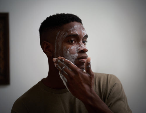 Man applying foaming facial cleanser on skin, showcasing skincare routine in a neutral setting.