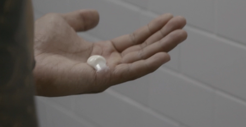 Close-up of a hand holding a small, white cream product suitable for skincare.